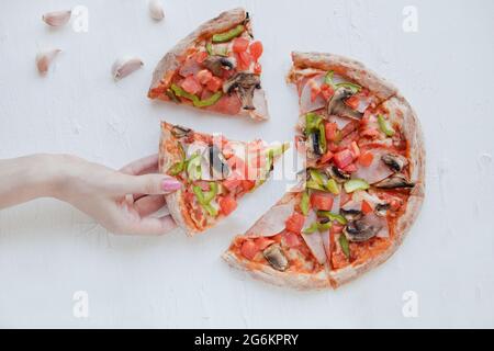 Frau Hand hält Pizza-Scheibe. Teilen Sie eine köstliche Pizza auf weißem Hintergrund, halten eine Scheibe, Draufsicht Stockfoto