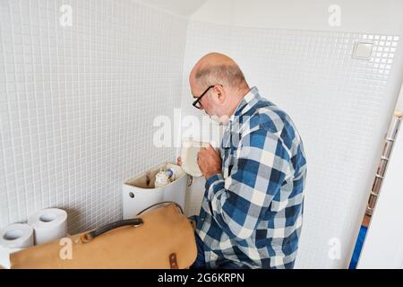 Klempner Handwerker repariert defekte Toilettenzisterne in der Toilette Stockfoto