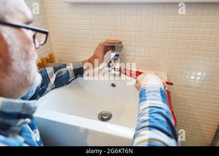 Handwerker Klempner montiert oder repariert Wasserhahn auf Waschbecken im Badezimmer Stockfoto