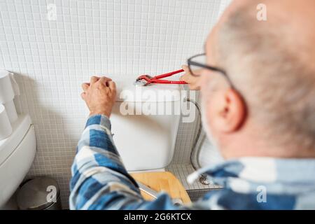 Installateur mit Rohrschlüssel repariert die Zisterne in der Toilette Stockfoto