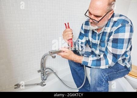 Ein Klempner als Handwerker repariert den Duschkopf und den Schlauch im Badezimmer Stockfoto