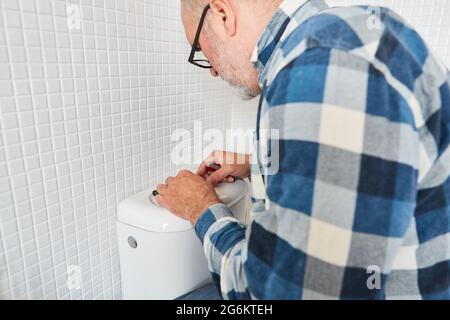 Handwerker Klempner repariert defekte Toilettenspülung auf der Zisterne in der Toilette Stockfoto