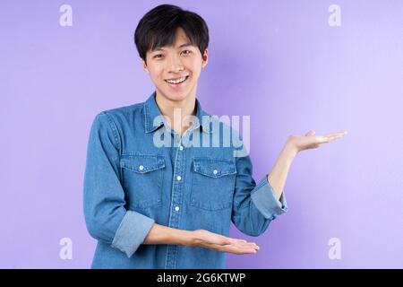 Porträt eines asiatischen Mannes in blauem Hemd, der auf purpurem Hintergrund posiert Stockfoto