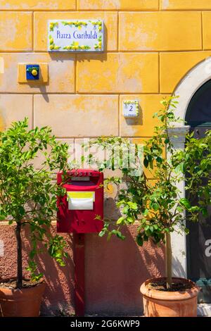 Alter roter italienischer Briefkasten auf einer gelben Wand mit Zitronenbäumen daneben und einem Straßenschild in der Stadt Limone am Gardasee in Italien Stockfoto