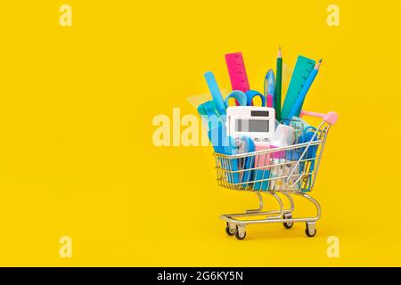 Schulpapiere in einem Einkaufswagen auf gelbem Hintergrund. Zurück zum Schulkonzept. Stockfoto