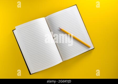 Offenes liniertes Notizbuch mit gelbem Bleistift isoliert auf gelbem Hintergrund in der Draufsicht, flach liegend, Kopierbereich Stockfoto