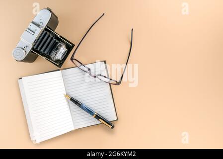 Retro-Kamera mit Notebook und altem Füllfederhalter und Brille auf hellbraunem Hintergrund, Reisekonzept, Kopierraum Stockfoto