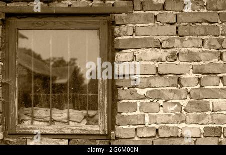 Alte Backsteinmauer mit einem Holzfenster. Mit Metallgittern. Anzeige eines alten Hauses im Fenster. Schwarz und Weiß. Stockfoto