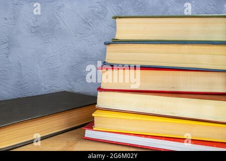 Stapel mehrfarbiger Hardback-Bücher auf Holztisch gegen grau-blaue Betonwand Stockfoto
