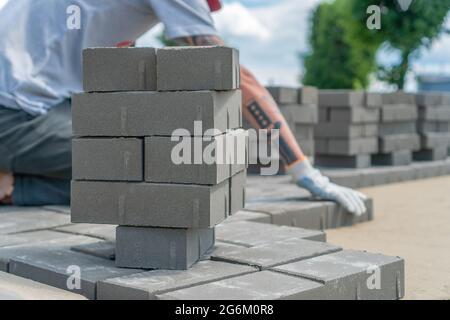 Nahaufnahme der Hände eines Bauarbeiters, die an einem sonnigen Sommertag Pflasterplatten im Freien auf einem vorbereiteten Fundament legen Stockfoto