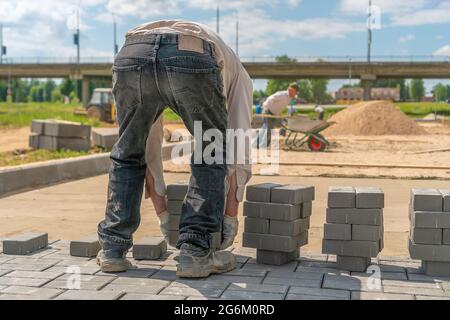 Der Arbeiter legt eine Menge Betonsteine auf den Boden. Verlegung von Pflasterplatten Stockfoto