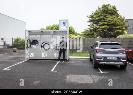 Ein Mann wartet auf seine Wäsche in einem Waschsalon im Freien auf einem Supermarkt-Parkplatz in Plousgasnou, Frankreich Stockfoto