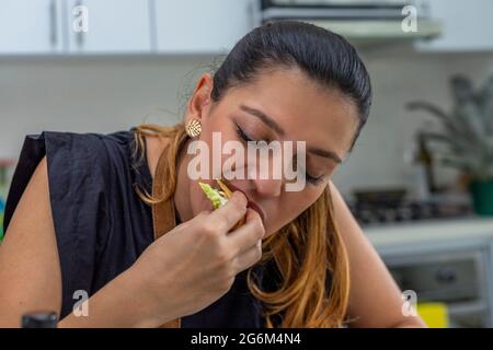 Junge Frau, die in der Küche einen frisch zubereiteten Taco isst Stockfoto