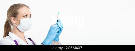 Eine junge Krankenschwester in einer Maske wählt den Impfstoff in eine Spritze, während sie in einem Krankenhaus neben einem Patienten sitzt. Patientin wartet auf Grippeinspritzung Stockfoto