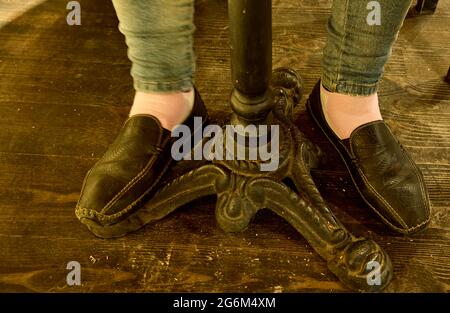 Frauenbeine in schwarzen Schuhen unter dem Tisch. Nahaufnahme, Tageslicht. Stockfoto