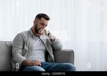 Deprimiert traurig attraktiver Mann weint zu Hause auf dem Sofa, fühlt sich einsam, müde und besorgt Stockfoto