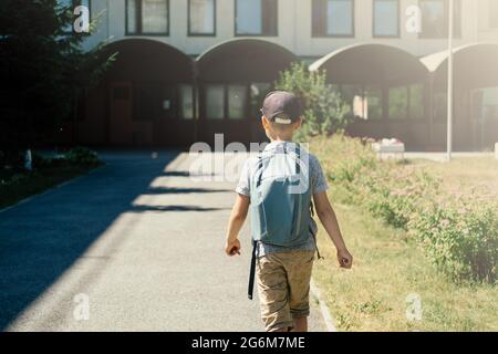 Der Junge, Grundschüler, zu Fuß zur Schule mit Tasche hinter dem Rücken und Buch. Die Studenten sind bereit für das neue Jahr. Zurück zur Schule. Stockfoto