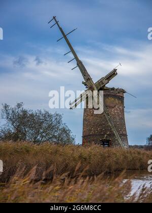 Blick über Feld und Wasser einer zerstörten Pumpwindmühle bei Horsey on the Boards in Norfolk England Stockfoto