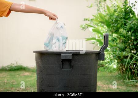 Hand von Menschen, die Müll in Plastiktüten in den Müll im Garten werfen. Stockfoto