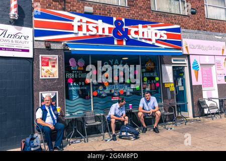 Drei Mann sitzen draußen und typisch britische Fisch- und Chipladen, die mit der Gewerkschaftsflagge Norwich England dekoriert ist Stockfoto