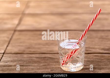 Glas Sodawasser mit rot-weiß gestreiftem Stroh auf Holztisch. Erfrischendes alkoholfreies Getränk für heiße Sommertage, um für eine Detox-Diät hydratisiert zu bleiben. Stockfoto