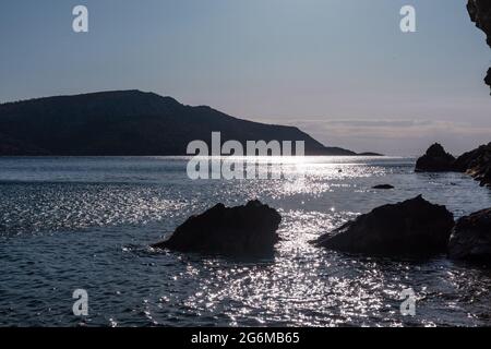 Die Sonne scheint an der wilden Küste des mittelmeers mit dunklen Felsen, Silhouetten, klarem Wasser und Sonnenstrahl. Reisen Sie nach Griechenland in der Nähe von Athen. Sommer Natur am Meer Stockfoto