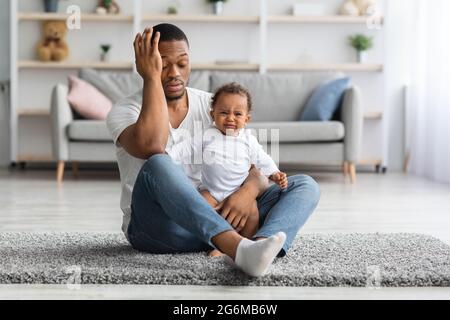 Erschöpfter Schwarzer Vater Sitzt Zu Hause Mit Weinenden Neugeborenen Auf Dem Boden Stockfoto