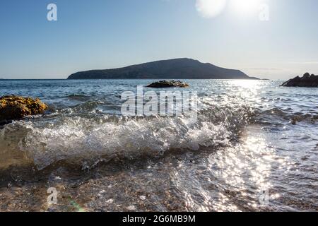 Die Sonne scheint auf weißen Wellen und trifft die wilde Küste aus nächster Nähe. Mittelmeer mit Felsen, klarem Wasser und Sonnenstrahl. Reisen Sie nach Griechenland in der Nähe von Athen. Sommersaison Stockfoto