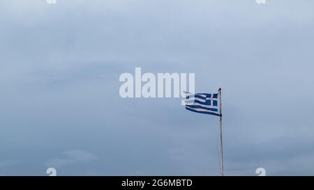 Flagge Griechenlands auf Fahnenmast winkt im Wind auf trübenem grauen Himmel mit Kopierraum. Nationales griechisches Symbol blau und weiß gestreift mit Kreuz Stockfoto