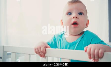 Überrascht Baby Junge stand in Baby Krippe und blickte auf Stockfoto