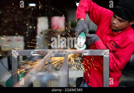 Schweißer verwendete Schleifstein auf Stahl in der Fabrik mit Funken, Schweißprozess in der Industriewerkstatt, Hände mit Instrument im Rahmen. Stockfoto