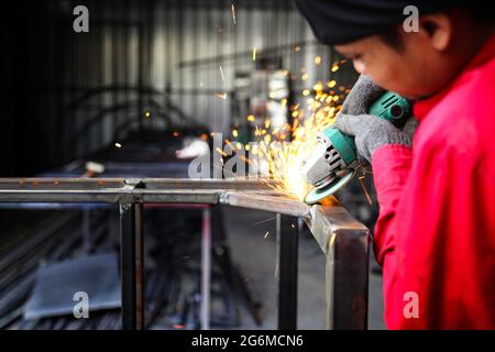 Schweißer verwendete Schleifstein auf Stahl in der Fabrik mit Funken, Schweißprozess in der Industriewerkstatt, Hände mit Instrument im Rahmen. Stockfoto