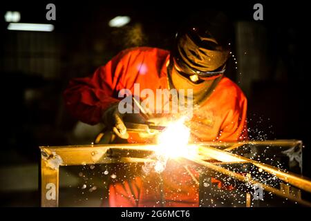 Schweißer verwendete Schleifstein auf Stahl in der Fabrik mit Funken, Schweißprozess in der Industriewerkstatt, Hände mit Instrument im Rahmen. Stockfoto