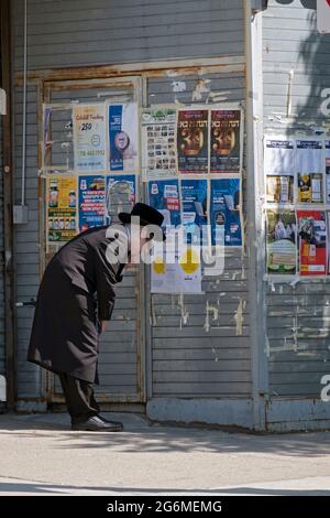 Ein junger orthodoxer Jude, wahrscheinlich ein Satmar, sieht sich Plakatwerbung an, die meist in Jiddisch ist. Auf der Lee Avenue in Williamsburg, Brooklyn, NYC Stockfoto