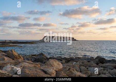 Felsige Küste von Agios Georgios Zypern. Blick auf die Insel Yeronisos. Sonnenuntergang am Hafen von Agios Georgios Pegeias in Paphos, Zypern. Die Halbinsel Akamas Stockfoto