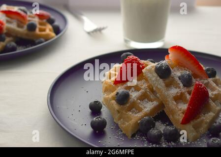 Morgens servieren wir ein Frühstück mit frisch gebackenen Waffeln und ebenso frischen Beeren. Alles unter einer dünnen Decke aus Puderzucker. Stockfoto