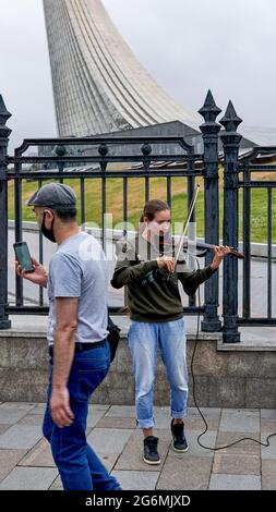 Moskau, Russland. Juni 2021. Ein Mann geht an einem Straßengeiger am Fuße des Monuments der Eroberer des Weltraums vorbei. (Foto von Mihail Siergiejevicz/SOPA Images/Sipa USA) Quelle: SIPA USA/Alamy Live News Stockfoto