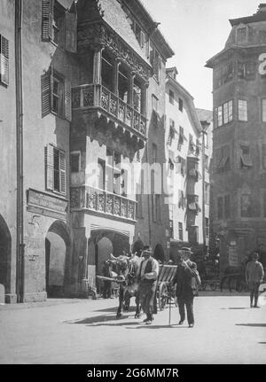 Ein Schwarzweißfoto aus dem frühen 20. Jahrhundert, aufgenommen in der Altstadt von Innsbruck, Österreich, zeigt das berühmte Goldene Dachl. Auf der Straße hat ein Mann einen Wagen, der von einer Kuh oder einem Stier gezogen wird. Stockfoto