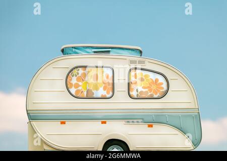 Vintage siebziger Jahre weißer Wohnwagen mit Blumenvorhängen vor einem blauen Himmel mit Wolken Stockfoto