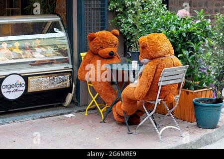 Große braune Teddybären, die an einem Tisch eines Straßencafés sitzen und darauf warten, serviert zu werden. Eisgefrierschrank im Hintergrund. Stockfoto