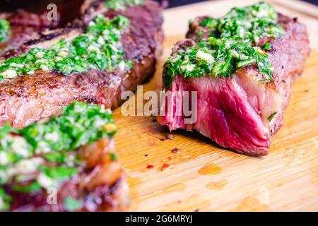 Argentinische gegrillte kurze Rippchen mit Chimichurri: Gegrillte, flankierte Rinderrippen auf einem Bambus-Schneidebrett Stockfoto