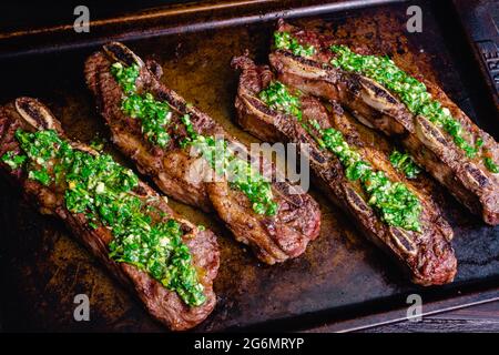 Argentinische gegrillte kurze Rippchen mit Chimichurri: Gegrillte, flankierte Rinderrippen mit Chimichurri-Sauce Stockfoto