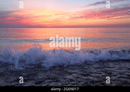 Das Licht des wunderschönen Sonnenuntergangs spiegelt sich auf dem Meer. Hohe Wellen mit Schaum breiten sich auf den Kieselsteinen an der Küste aus. Touristische Lage Stadt Batumi - Kopf Stockfoto