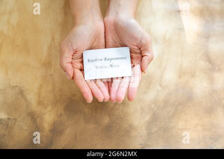 Hand mit Eid-al-Adha-Karte („Happy Feast of Sacrifice“ auf der Karte, die in türkischen Schriftstellern geschrieben wurde,) Stockfoto