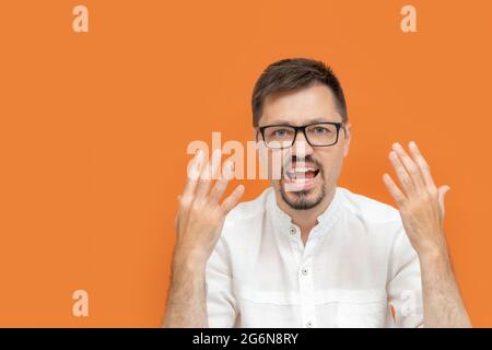 Ein hübscher Mann, der ein weißes Hemd und eine Brille trägt, schreit und winkt mit den Händen, steht auf einem orangefarbenen Hintergrund Stockfoto