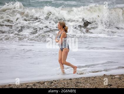 Portreath,Cornwall,7. Juli 2021,Trotz des grauen und trostlosen Wetters waren einige Leute bei Flut am Strand in Portreath, Cornwall. Eine Dame ging in einem Badeanzug am Strand entlang, obwohl es kühl war.Quelle: Keith Larby/Alamy Live News Stockfoto