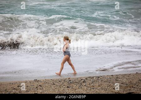 Portreath,Cornwall,7. Juli 2021,Trotz des grauen und trostlosen Wetters waren einige Leute bei Flut am Strand in Portreath, Cornwall. Eine Dame ging in einem Badeanzug am Strand entlang, obwohl es kühl war.Quelle: Keith Larby/Alamy Live News Stockfoto