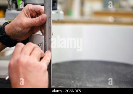 Der Zimmermann markiert das weiße Stück mit einem Bleistift und einem Lineal. Holzverarbeitende Industrie. Verarbeitungsanlage Für Acrylstein Stockfoto