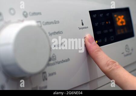 Foto einer Frau, die die Waschmaschine aufstellt, die Waschparameter anpasst und die Wäsche anmacht Stockfoto