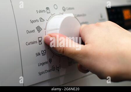 Foto einer Frau, die die Waschmaschine aufstellt, die Waschparameter anpasst und die Wäsche anmacht Stockfoto